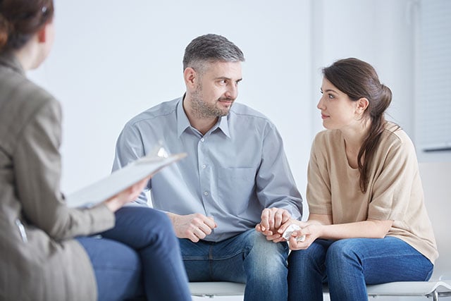 Couple engaged in marriage counseling session with therapist, focusing on communication and relationship support in a therapeutic setting.