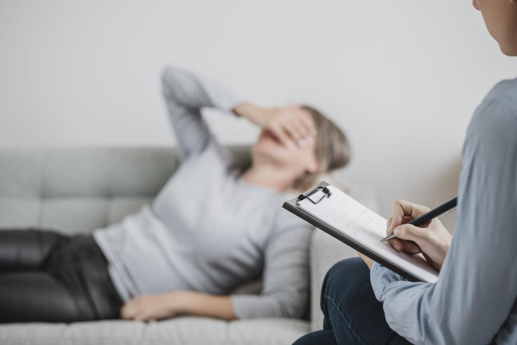 Therapist taking notes while a distressed client covers their face, illustrating anxiety therapy for various age groups in a counseling session.
