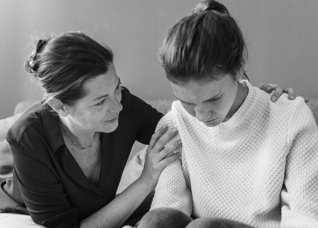 Mother comforting anxious adolescent during therapy session, addressing emotional challenges related to trauma and gun violence.