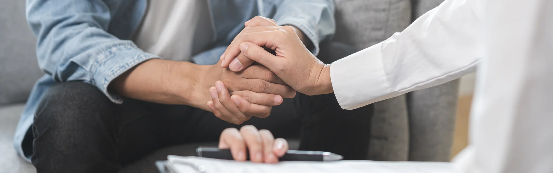 Hands of a therapist and client clasped together, symbolizing support and connection during trauma therapy sessions in a comfortable setting.