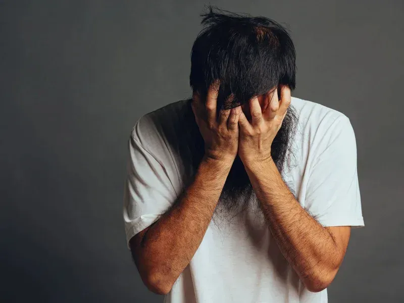 Man with long hair holding his head in distress, illustrating emotional signs of anxiety such as persistent worry and feelings of hopelessness.