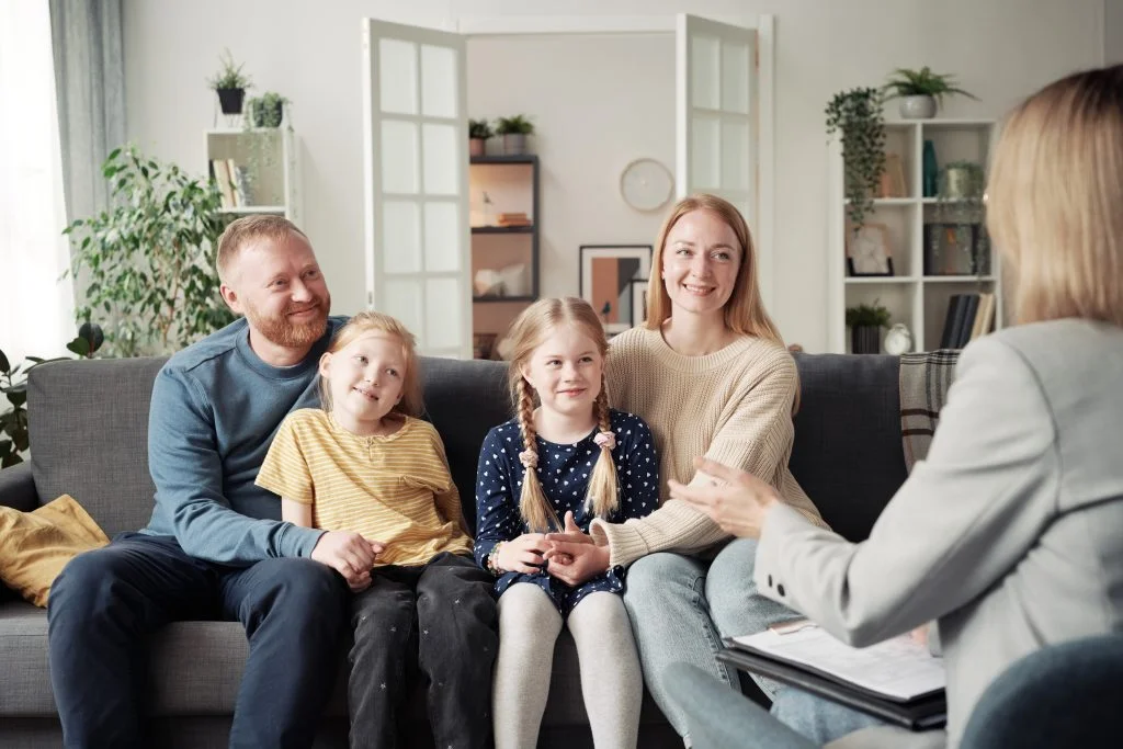 Family sitting together on a couch during a therapy session, engaging with a therapist, emphasizing communication and support in family dynamics.