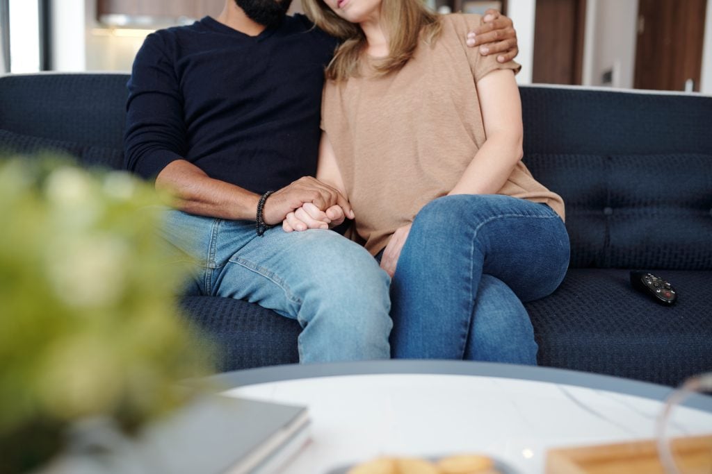 Couple sitting close on a couch, holding hands, symbolizing support and connection in marriage counseling.